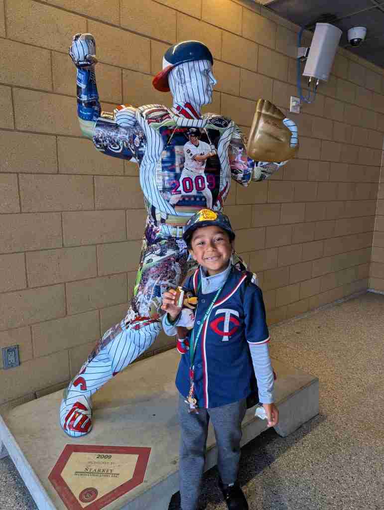 Smiling boy in a Twins jersey beside a painted Joe Mauer statue at Target Field